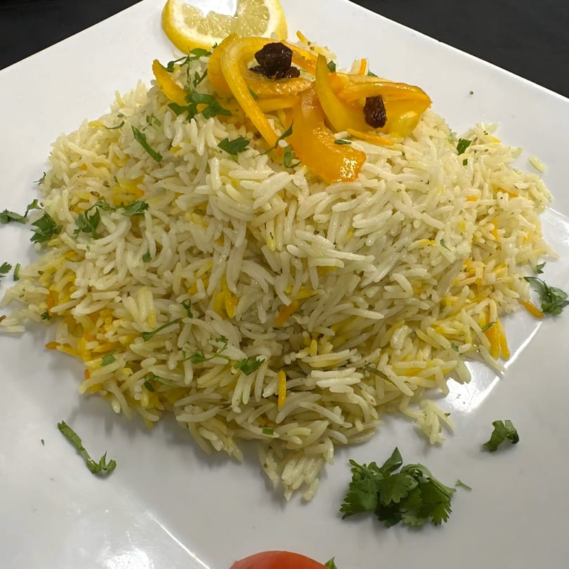A plate of African-style rice, garnished with yellow bell pepper strips, raisins, cilantro, and a lemon slice.
