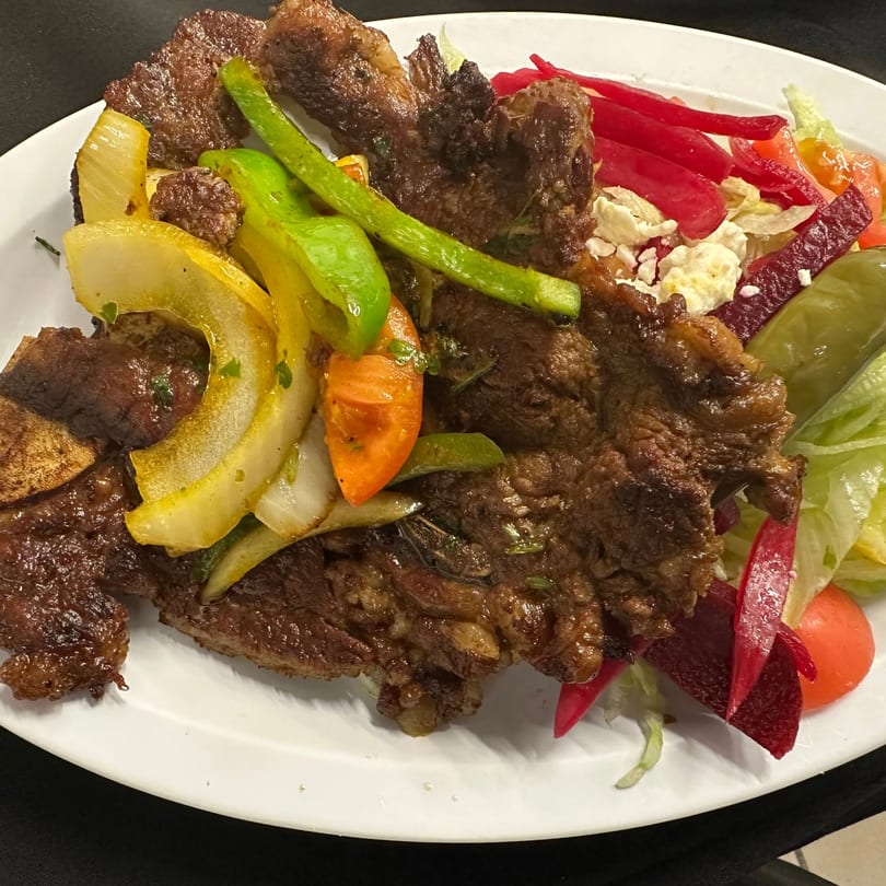 African-style grilled meat with sautéed onions, peppers, and a side salad with feta cheese.