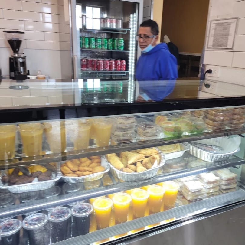 A man in a blue hoodie stands behind a Quruxley Restaurant display case filled with African food and drinks.