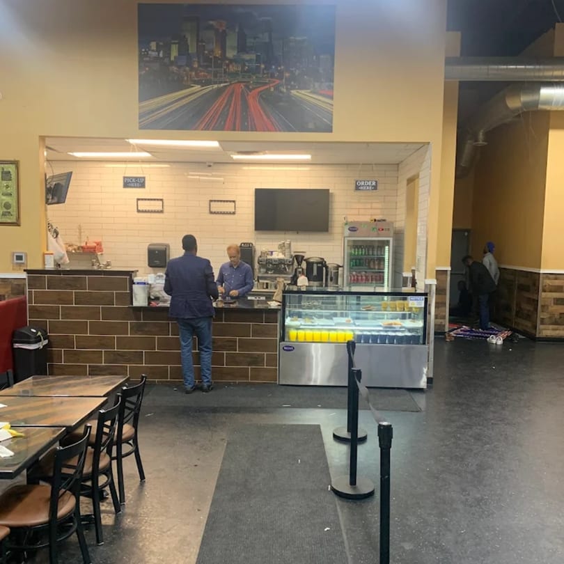 A customer orders at the counter of Quruxley Restaurant, with a city skyline mural above.