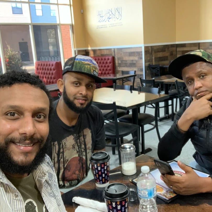 Three men smiling at the camera, seated at a table in Quruxley Restaurant.
