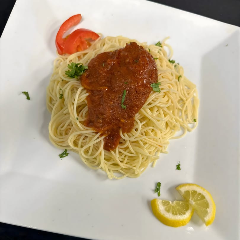 Spaghetti with red sauce, garnished with parsley, tomato, and lemon wedges on a white plate.