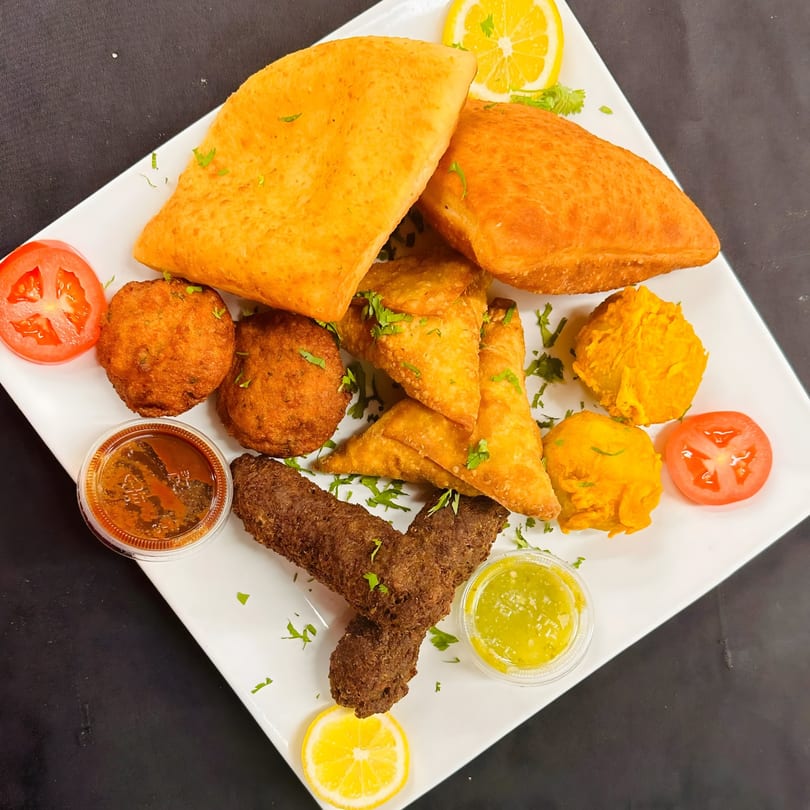 A white platter filled with various African appetizers, including samosas, fried dough, and meatballs.